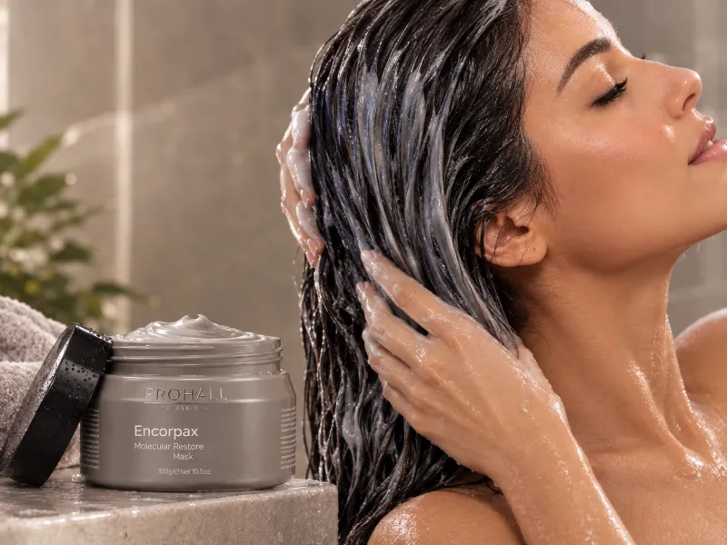 Mulher espalhando a máscara no comprimento dos fios molhados, ao lado do pote da Máscara Encorpax Molecular Restore